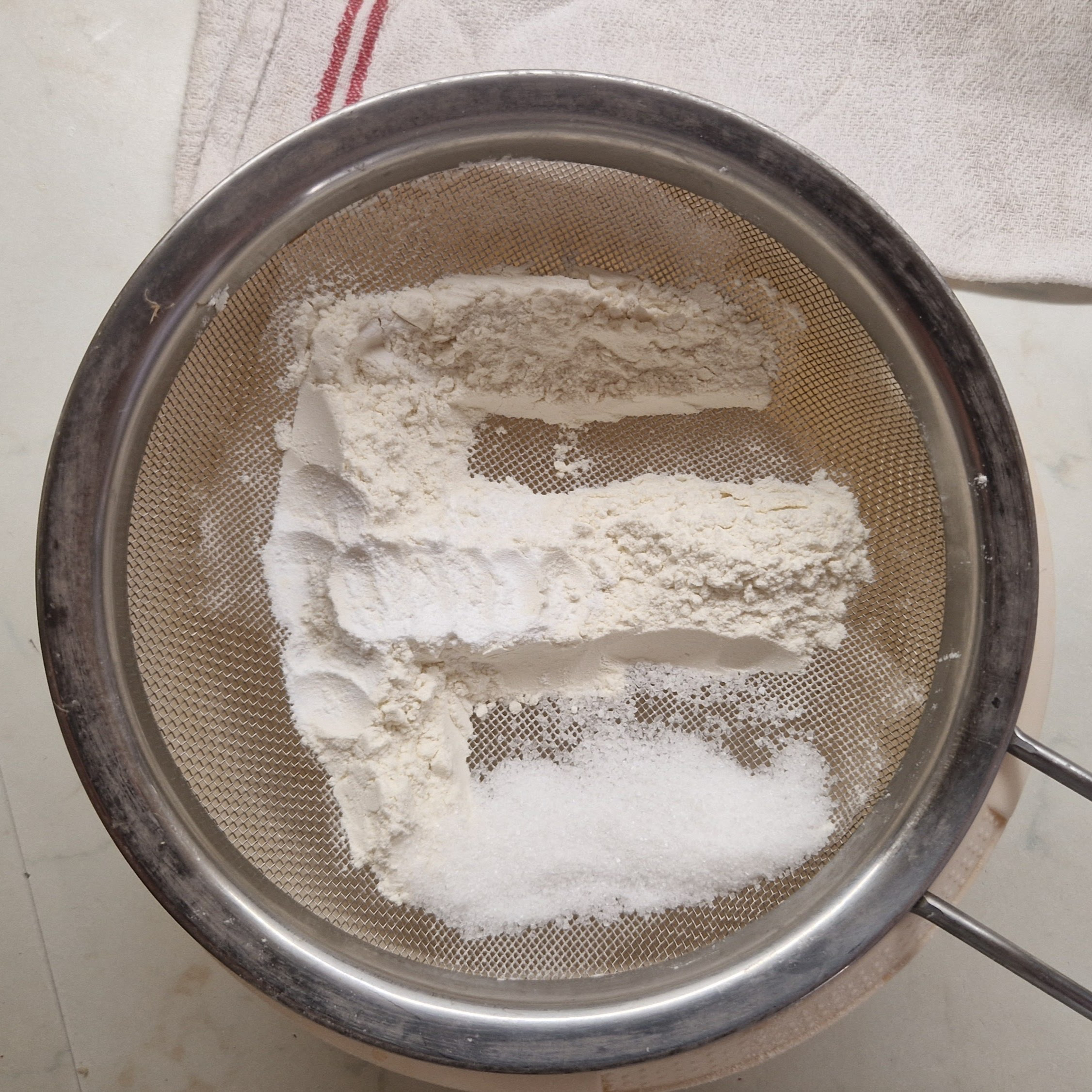 Flour, sugar, salt and baking powder on a sive formed into E